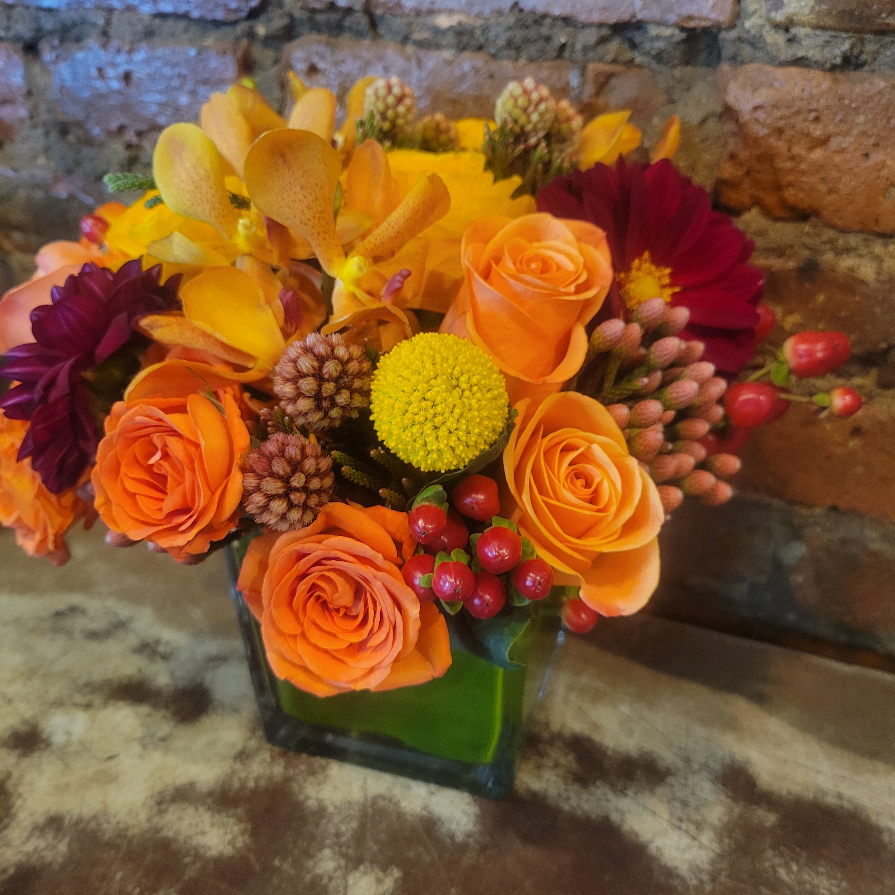 arrangement wit orange roses , crapedia orchids and berries