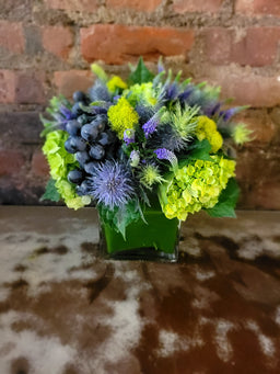 arrangement with blue thistle , green hydrangea grapes and moss